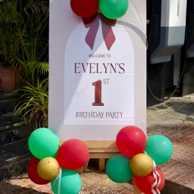 A festive welcome sign for Evelyn's Christmas-themed first birthday party, decorated with red, green, and gold balloons.