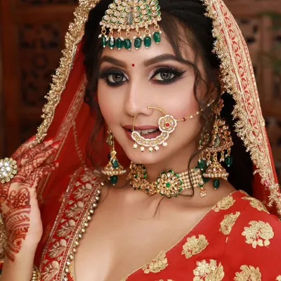 A quintessential high-glam bridal look. The combination of smokey eyes, a flawless base, and a red lehenga is a classic that never fails.