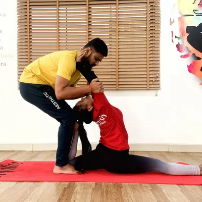 Assisting a student in a deep split pose, Hanumanasana, requires careful support to protect the muscles while encouraging greater flexibility.