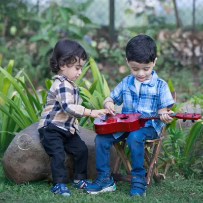 Two little brothers share a sweet moment with a toy guitar in a lush garden. One teaches the other, showing the curiosity and connection that defines siblinghood.