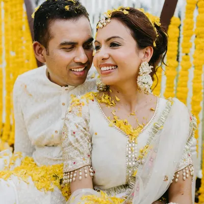 A sweet, candid moment of a couple during their Haldi, surrounded by marigold flowers, sharing a happy and intimate glance.