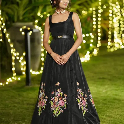 Actress Divya Shree from Australia in a custom-made black raw silk gown. The gown features a square neckline and is adorned with colorful floral hand embroidery at the hem.