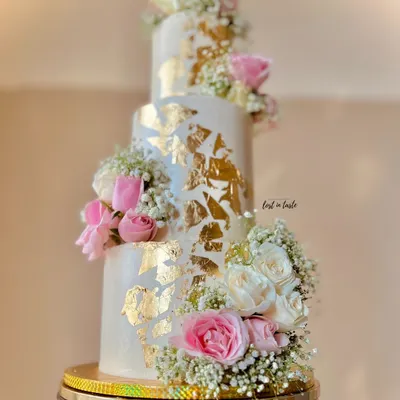 A beautiful three-tiered engagement cake with cascading fresh roses and baby's breath. The gold leaf accents and custom monogram add a touch of personalized luxury.