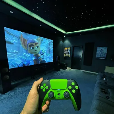A first-person view of a gaming session in a custom-built room. The setup includes a massive screen, tower speakers, and a fiber-optic starfield ceiling to create a completely immersive environment.