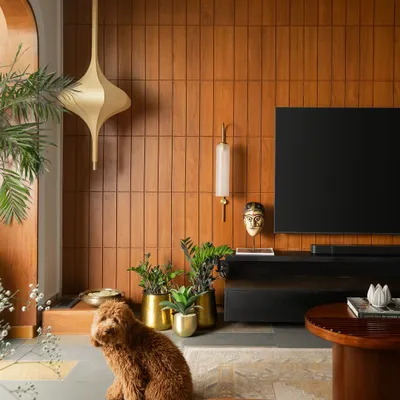 In this home inspired by Indian heritage, the living area features a teak veneer wall with brass accents as a warm backdrop. The space is grounded by a fusion of polished and unpolished Kota stone flooring with Jaisalmer marble inlays.