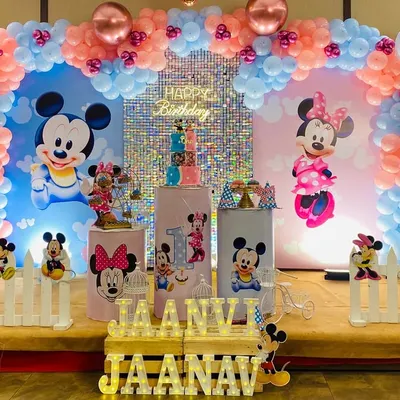 A grand Mickey and Minnie Mouse theme for a twin's first birthday. The stage is split into blue and pink sections, each with large character backdrops, a shimmer wall, and personalized props.