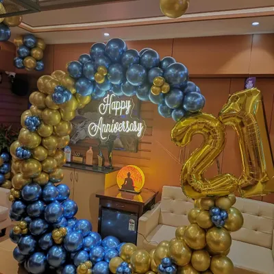 A grand 21st-anniversary celebration. This decor features a stunning circular balloon garland in metallic blue and gold, a 'Happy Anniversary' neon sign, and large foil numbers to highlight the milestone.