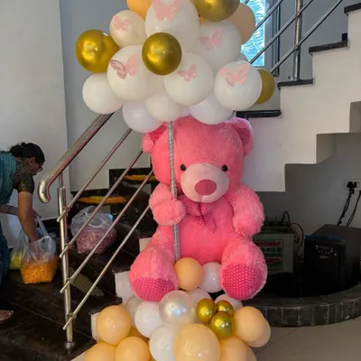 A cute welcome prop for a butterfly-themed party, featuring a large pink teddy bear holding a bunch of balloons with butterfly prints.
