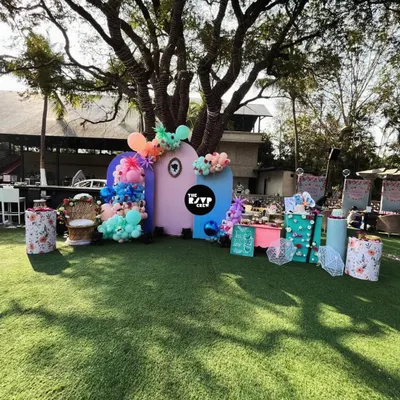 For this outdoor baby shower, we created a fun and colorful backdrop on a lush green lawn. The setup features abstract pastel panels, vibrant balloon clusters, and a dedicated dessert table, all centered around a large tree for a playful, natural feel.