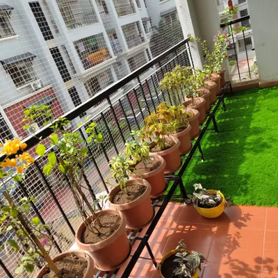 A perfect example of a functional and beautiful apartment balcony. The design uses artificial grass for easy upkeep, planters on stands to maximize floor space, and a full-coverage safety net, making it a safe and green spot to relax.