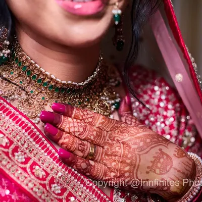 This shot is dedicated to the beautiful details of the bridal look. It highlights the stunning green and gold necklace, the intricate mehendi, and the rich texture of her red lehenga.