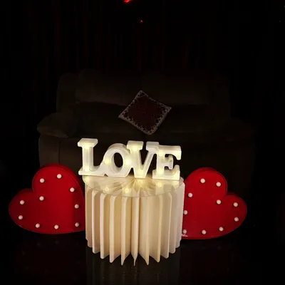 Simple, classic, and romantic. This setup features a 'LOVE' marquee sign flanked by two light-up hearts, creating a perfect focal point for an anniversary or proposal in a dimly lit, intimate setting.