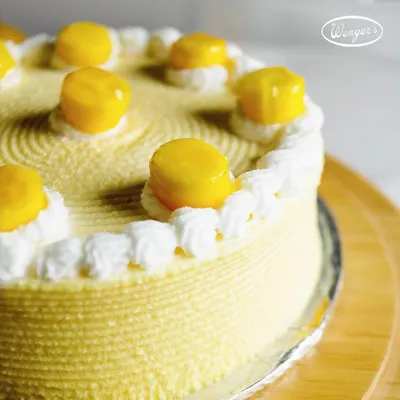 A close-up of our seasonal Mango Cake. The sides are beautifully textured, and the top is adorned with dollops of fresh cream and sweet, juicy mango pieces. It’s a simple, elegant cake that lets the fruit shine.