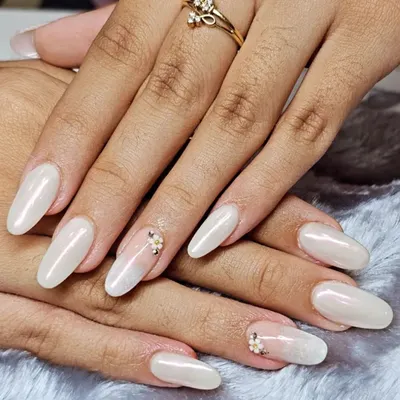A stunning example of long, almond-shaped nail extensions with a pearlescent white finish. To make it special, I added a tiny, hand-placed floral gem cluster on the ring finger for a subtle and elegant accent.