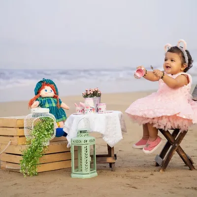 A tea party for two on the beach, with a special doll as the guest. The soft morning light and ocean backdrop create a magical setting for this outdoor shoot.