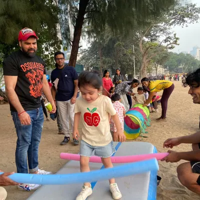 A toddler carefully navigates a balance challenge with help from our coaches and his dad. Our beach parties are designed for all ages, focusing on building confidence through play.