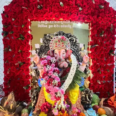 A beautiful pink and red rose kanthi I made, seen here adorning a Ganpati idol during a festival. The garland is set against a stunning backdrop of red roses.