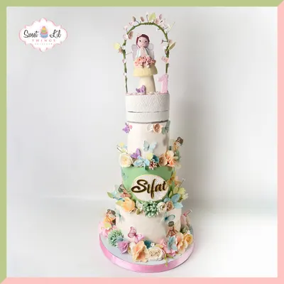 A fairytale in frosting! This grand, multi-tiered cake for Sifat's first birthday features a garden of pastel flowers, butterflies, and a sweet little fairy on top.