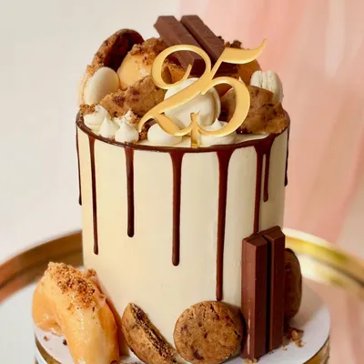 A close-up of my popular loaded drip cake for a 25th birthday. You can see the rich chocolate drip, cookies, donuts, macarons, and a custom gold topper.