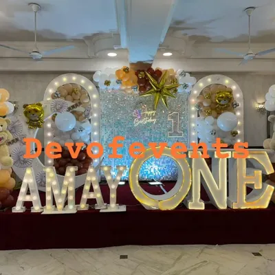 A grand stage for a teddy bear themed first birthday. This setup features a silver sequin shimmer wall, large light-up marquee letters for the name and age, and balloon arrangements in white, brown, and gold.