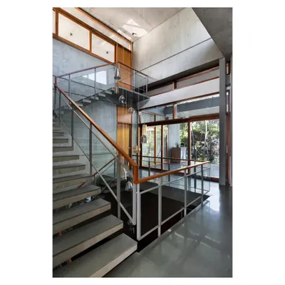The cantilevered concrete staircase in the 'House of Canopies' is a feat of engineering and a central sculptural element. It appears to float against the raw concrete walls, connecting the different levels of the triple-height space.