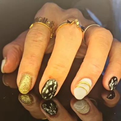 A chic and contrasting manicure featuring gold glitter, black and white patterns, and gold striped accents.