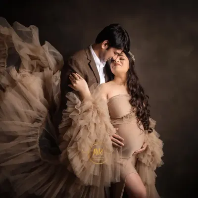 An intimate moment between an expecting couple. The flowing fabric of the gown adds a touch of drama and elegance to this maternity portrait against a classic dark backdrop.