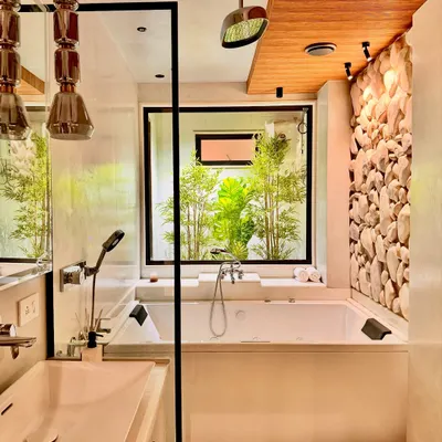 In this biophilic bathroom design, I wanted to blur the line between inside and out. A large window looks out onto a private bamboo garden, bringing a sense of nature directly into the space. The design features a jacuzzi bathtub, a pebble-stone accent wall, and a wooden ceiling to create a complete sensory experience of a luxury home spa.