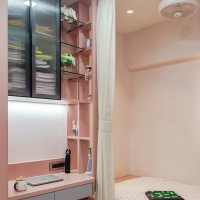 This compact room is designed to be highly functional, with a cozy bed nook separated by a curtain from a dedicated study area. The custom pink joinery includes a desk, open shelving, and glass-fronted overhead cabinets for ample storage.