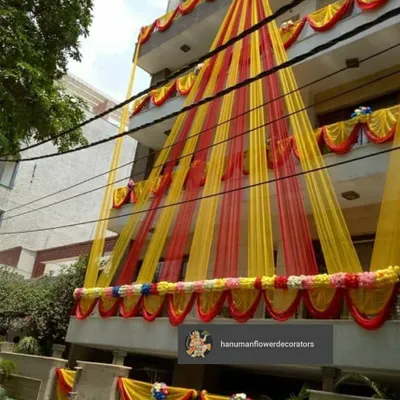 I make sure the festive feeling starts right at the entrance. This is an exterior decoration for a multi-story residence, using bright yellow and red drapes and floral arrangements to make the entire building look ready for a celebration.