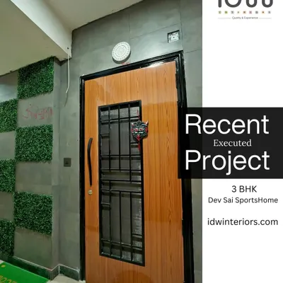 A modern entrance at Dev Sai SportsHome. The door features a wood finish with a metal grill, complemented by a concrete-texture wall and artificial green panels for a unique look.