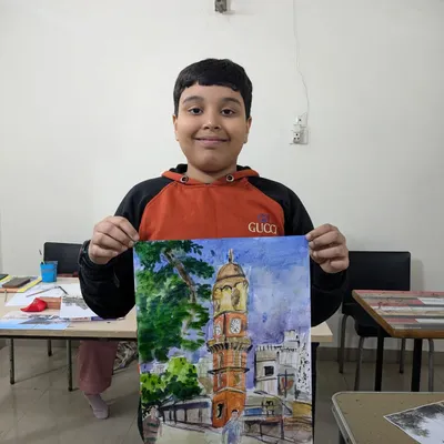 A student proudly holding his watercolor painting of a clock tower. This landscape piece shows a good understanding of perspective, color mixing, and architectural detail.