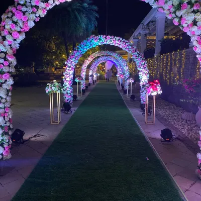 The same beautiful floral arches from the daytime, now transformed for the evening with dramatic uplighting. This creates a completely different, more glamorous atmosphere for a nighttime reception entrance.