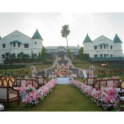 The stage is set for a fairytale wedding in the hills of Mussoorie. The aisle, lined with lush pink and white florals, leads to a mandap with the majestic Savoy palace as its backdrop, promising a ceremony of unparalleled beauty.