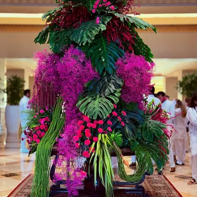 A symphony of pink and green. This large-scale lobby arrangement combines lush monstera leaves with vibrant pink orchids and cascading foliage to create a tropical yet elegant statement piece.