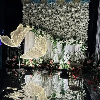 A whimsical and dreamy photo booth. We created this with a wall of white flowers, glowing butterfly installations, and a reflective floor for a magical effect.