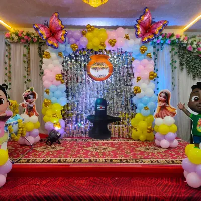 A colorful naming ceremony decoration featuring a shimmer wall, pastel balloon pillars, and Cocomelon character cutouts.