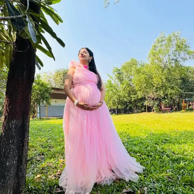 A beautiful solo portrait taken in a garden setting. The natural sunlight and green background make this pink maternity gown look even more vibrant and beautiful.