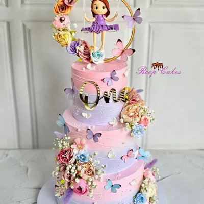 A whimsical and dreamy three-tier cake for a magical first birthday. This pastel creation is adorned with delicate butterflies, blooming florals, and an adorable fondant girl on a swing.