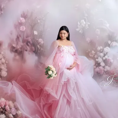 A dreamy, ethereal portrait of a mother-to-be in a flowing pink gown, surrounded by a magical fog and floral arrangement. This is a perfect example of a fantasy-style fine art shoot.