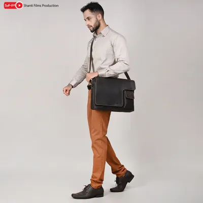 This lifestyle shot showcases a men's leather messenger bag in a professional context. The walking pose demonstrates the bag's size and how it's worn, helping customers gauge its practicality.