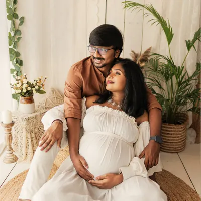 A perfect example of a boho-inspired maternity session. The couple relaxes on a jute rug, surrounded by plants and natural textures, creating a warm and earthy vibe.