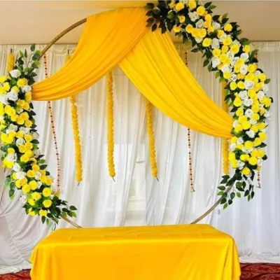 A beautiful Haldi ring backdrop with yellow and white flowers, perfect for an elegant ceremony. The setup includes a table covered in matching yellow fabric for placing ritual items.