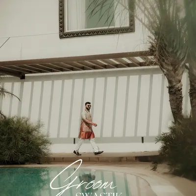 A stylish shot of the groom walking by the poolside. This captures his cool, relaxed demeanor and fashionable attire, a perfect portrait for a destination wedding.