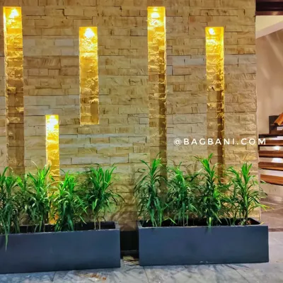 We designed this stunning entrance by pairing lush Dracaena plants with modern, dark planters. The arrangement is highlighted by warm accent lighting against the stone wall, creating an elegant and inviting atmosphere.