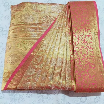 A close-up of a pre-pleated and folded silk saree in gold and pink. The pleats are perfectly aligned and pressed, showcasing the neatness of the final folded product.