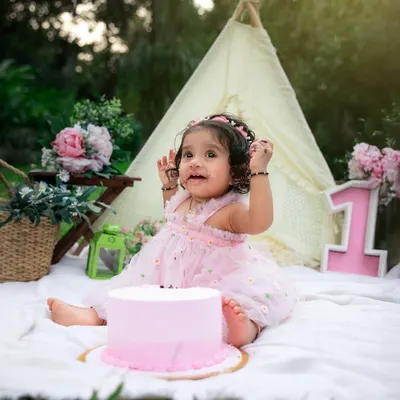 The best part of a cake smash is getting messy. This little princess is enjoying her first birthday cake in a beautiful garden setting, a perfect theme for an outdoor celebration.