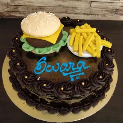 A cake that looks good enough to be a meal! This novelty cake features a meticulously sculpted fondant burger and a side of fries on top of a rich chocolate cake, perfect for a fast-food lover.