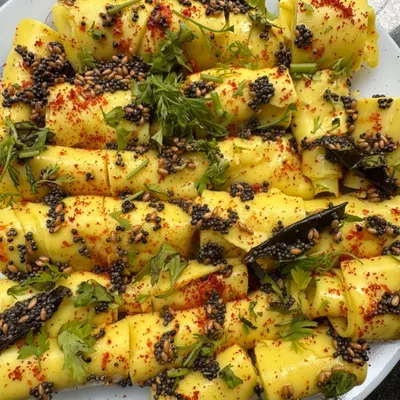 A platter of our delicate, paper-thin Khandvi rolls. These savory gram flour snacks are seasoned with mustard seeds, sesame seeds, and fresh cilantro, making them melt-in-your-mouth delicious.