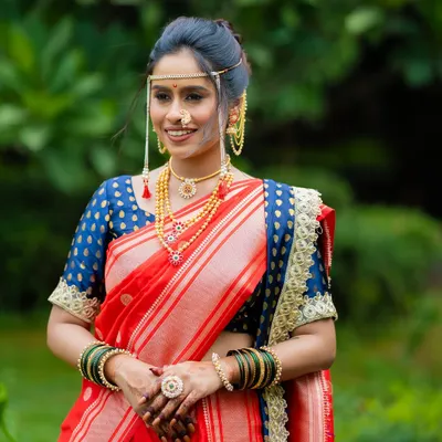 A classic Maharashtrian bridal look featuring a vibrant red Paithani saree. The makeup is kept minimal and radiant to highlight her natural features, complete with traditional jewelry like the mundavalya and nath.